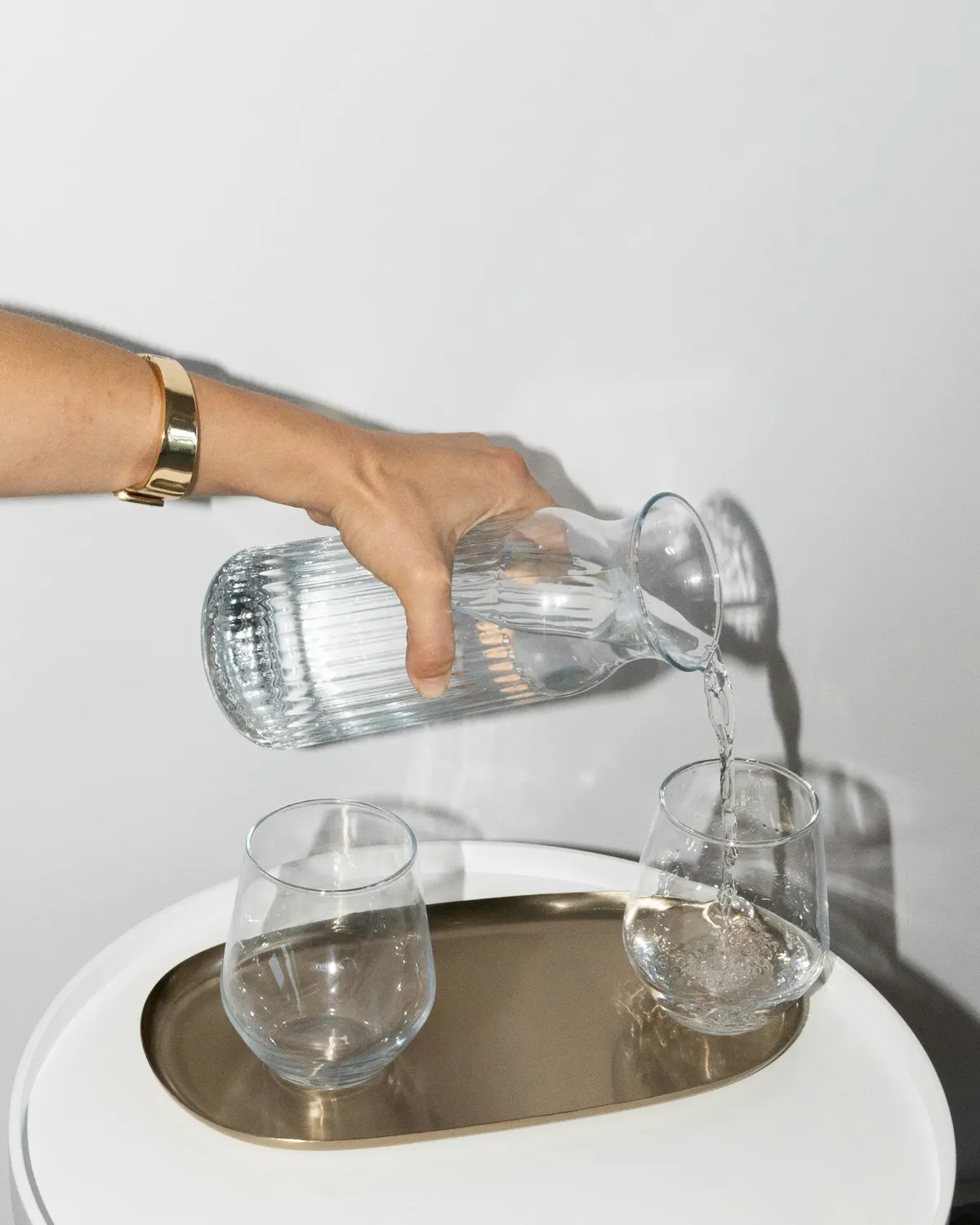 Une main verse l'eau d'une carafe en verre dans des verres, en lumière naturelle